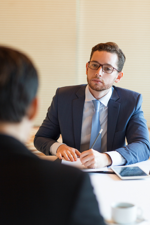 Closeup of serious middle-aged business man sitting at desk and interviewing unrecognizable applicant who is sitting back to camera in office